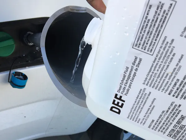 A worker is filling diesel exhaust fluid into the vehicle's filling port.