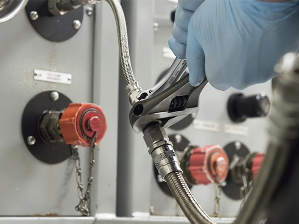 A worker is tightening the hydraulic fitting with a wrench.
